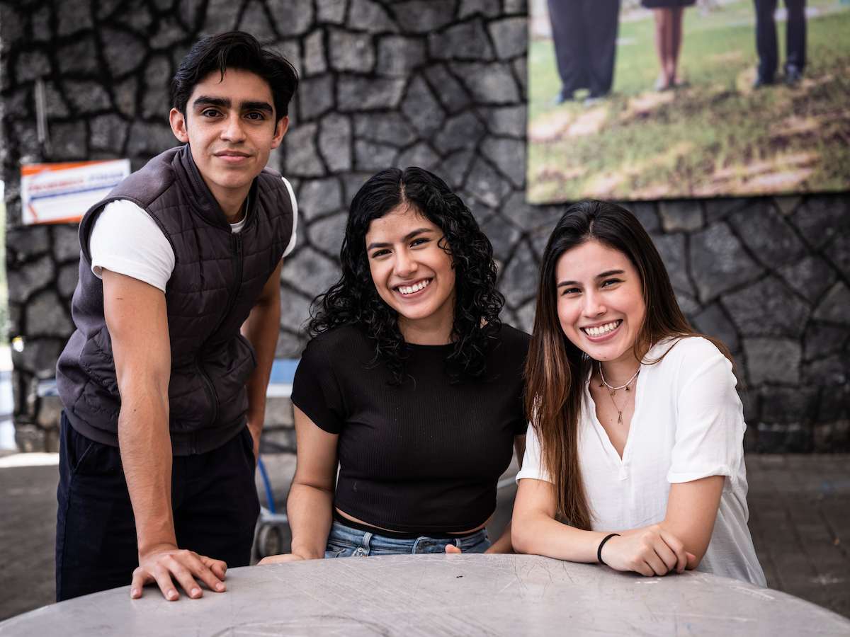 Tres estudiantes sonrientes en un espacio abierto universitario, reflejando empatía, cercanía y trabajo colaborativo en el contexto de la Licenciatura en Desarrollo Humano y Familiar.