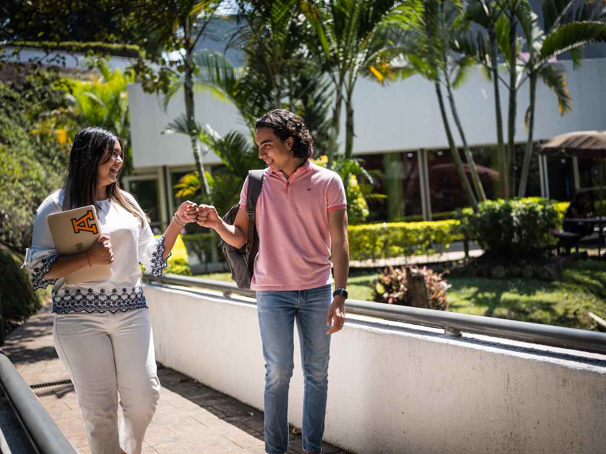 Estudiantes de la Licenciatura en Responsabilidad Social y Sustentabilidad caminando en el campus y saludándose con el puño, reflejando compañerismo, compromiso social y un entorno sustentable.