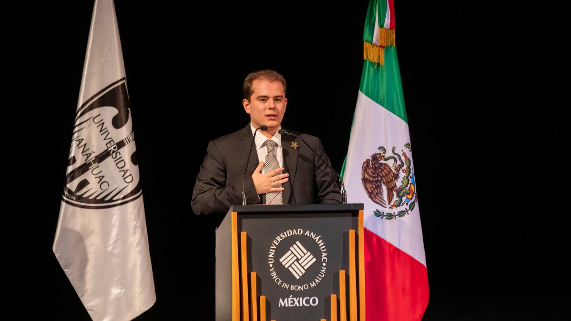 Estudiante de la Anáhuac trajeado dando un discurso sobre qué son las políticas públicas en un estrado