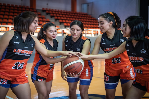 Alumnas de la Anáhuac en cancha de basquétbol sosteniendo el balón en el centro como equipo