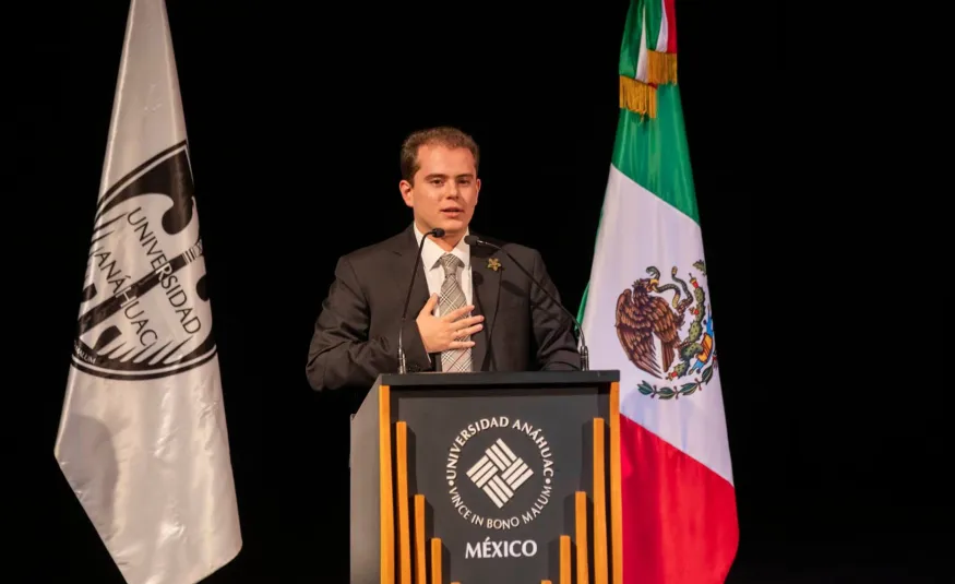 Estudiante de la Anáhuac trajeado dando un discurso sobre qué son las políticas públicas en un estrado
