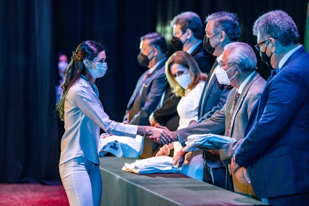 Alumna de Médico Cirujano recibiendo su bata blanca de uno de los doctores del presídium.