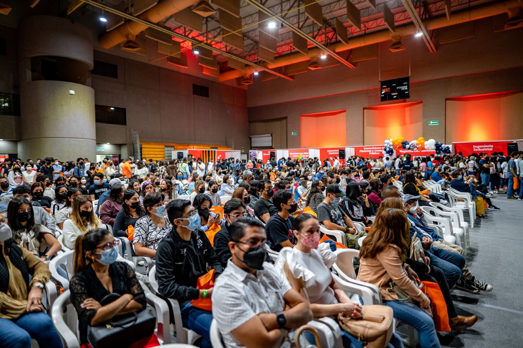 Multitud en el gimnasio, sentados, prestando atención.