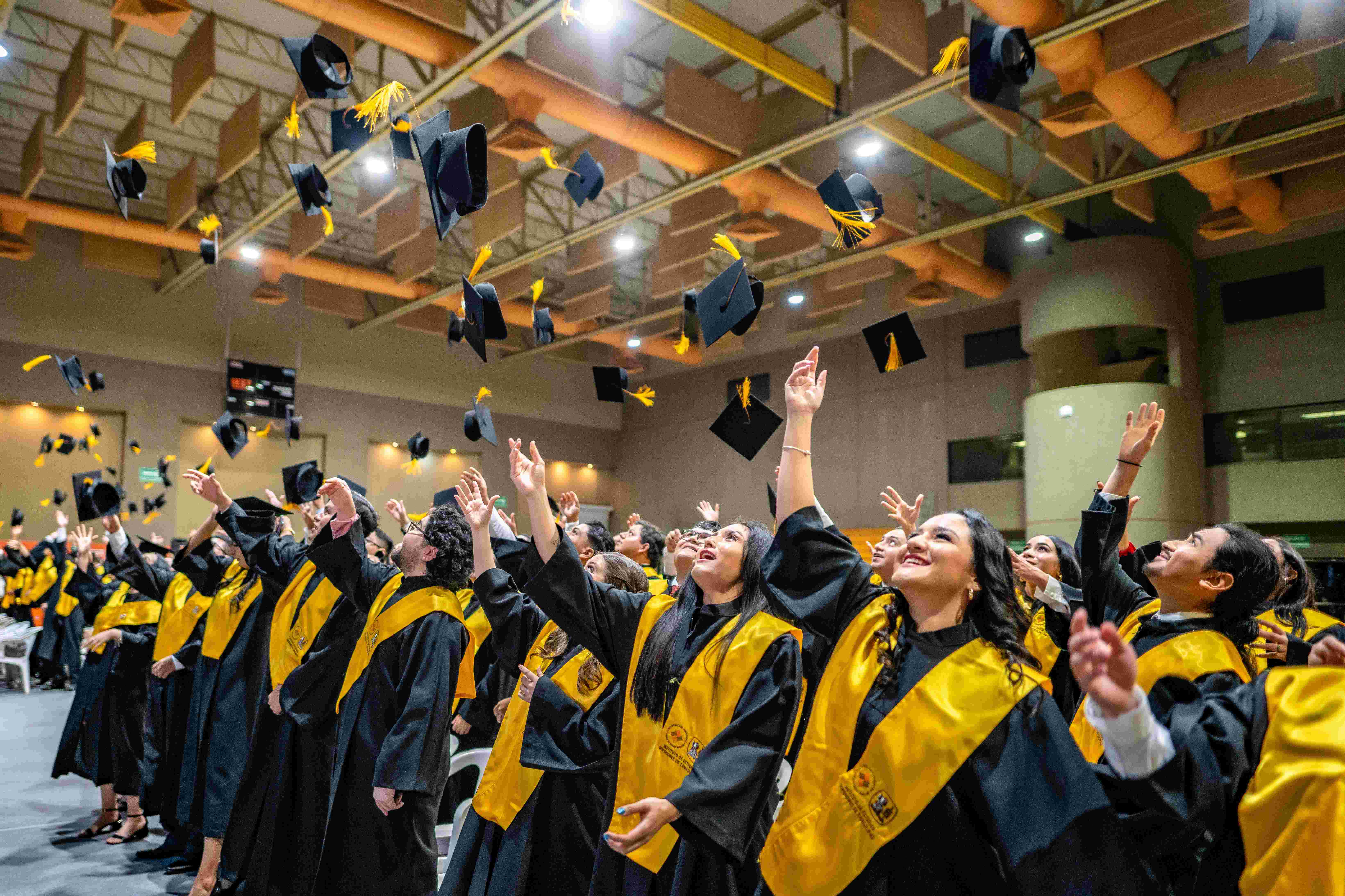 Alumnos de licenciatura aventando sus birretes al aire con cara de satisfacción.