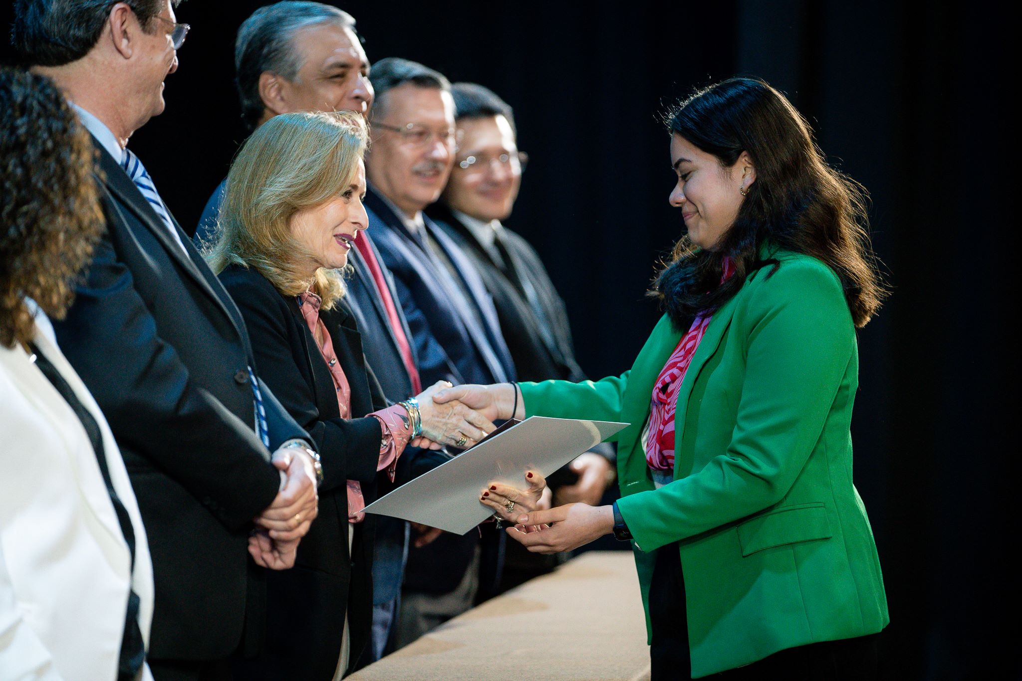 Egresada vestida de verde, recibiendo su diploma de CENEVAL.