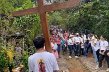 foto de un joven de espaldas sosteniendo una cruz, mientras al fondo se observa una multitud.