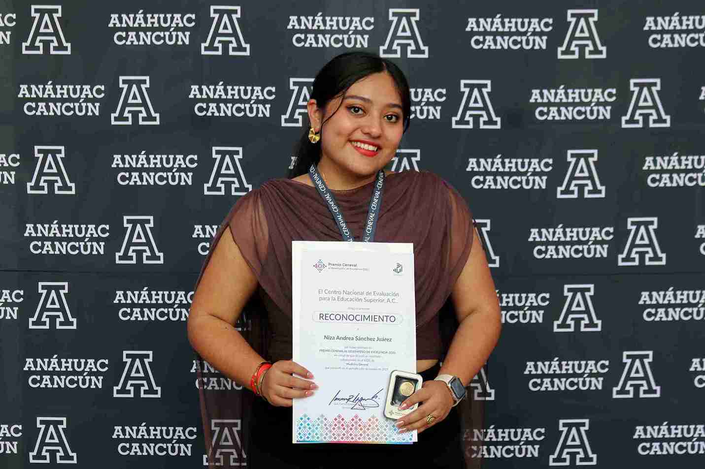 "Niza Andrea Sánchez Juárez sonriendo con su Reconocimiento de Excelencia Ceneval frente al muro institucional de la Universidad Anáhuac Cancún"
