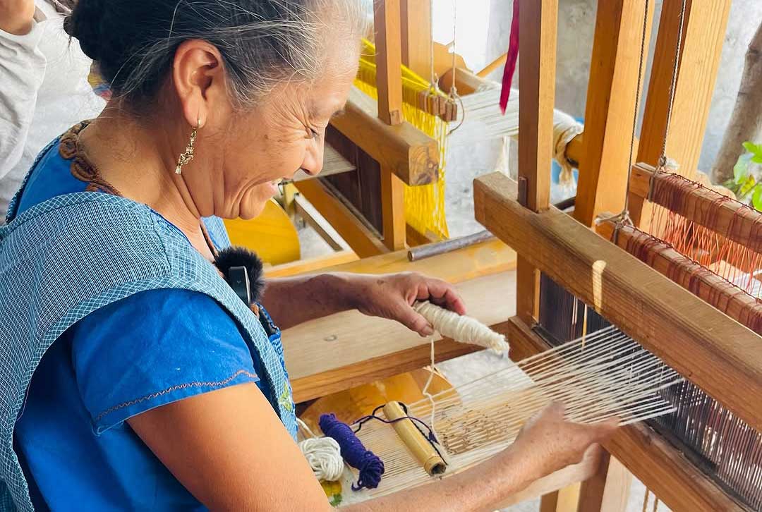 "Mujer artesana tejiendo hilos de lana en un telar de pedal tradicional"