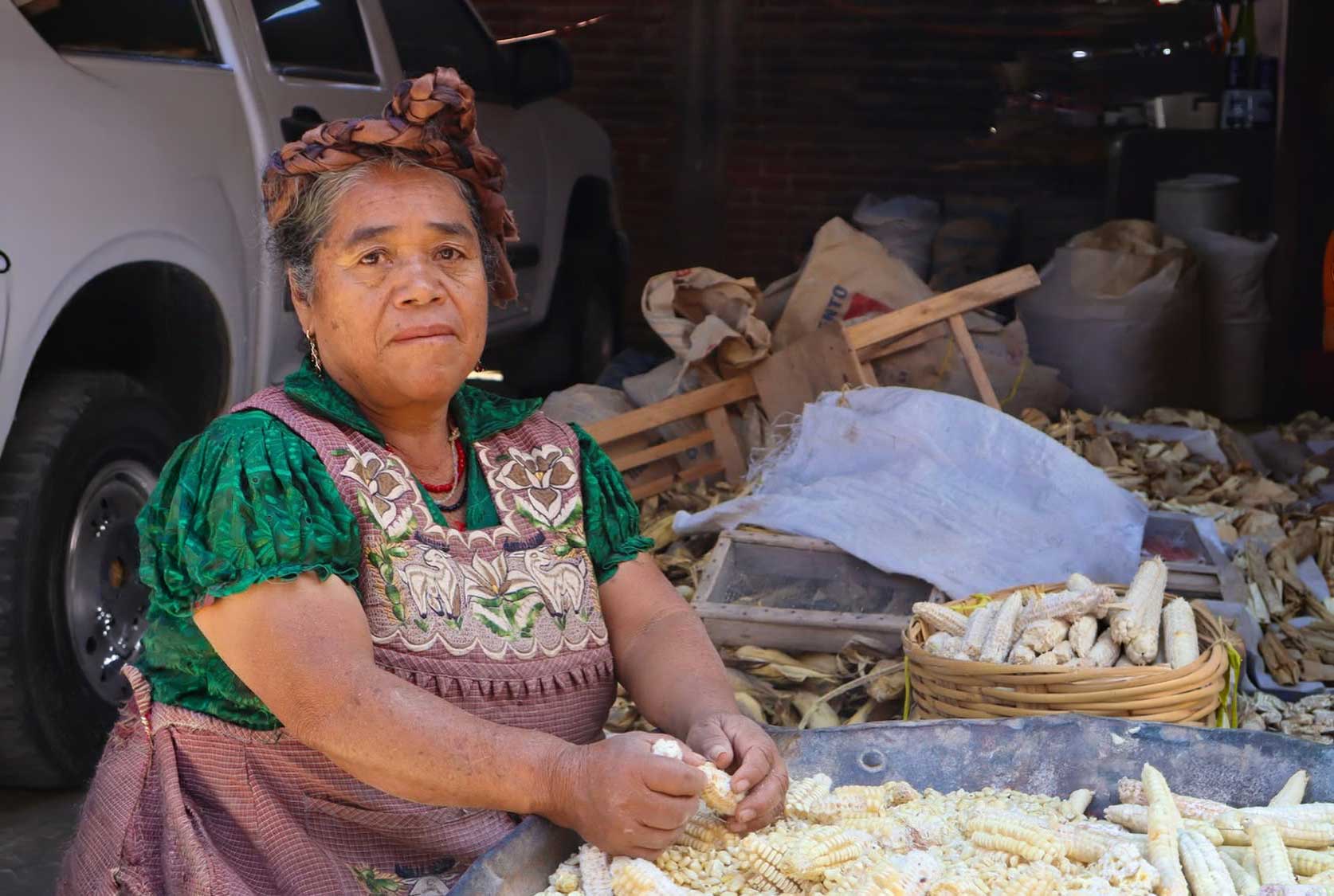 "Mujer indígena desgranando maíz blanco en un mercado tradicional mexicano"