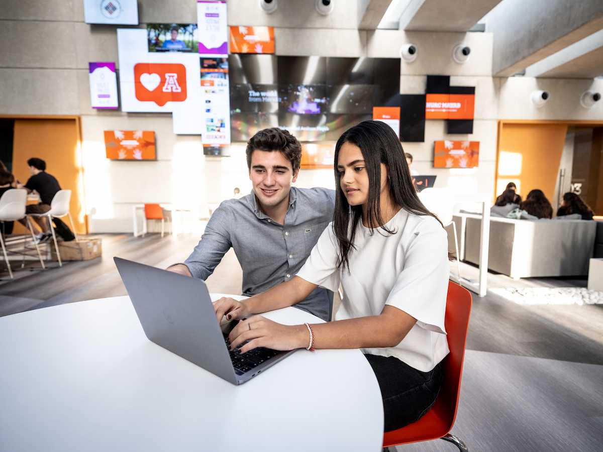 Estudiantes de Inteligencia Estratégica trabajando en equipo frente a una laptop en un entorno moderno, reflejando análisis colaborativo, pensamiento crítico y uso de herramientas digitales.